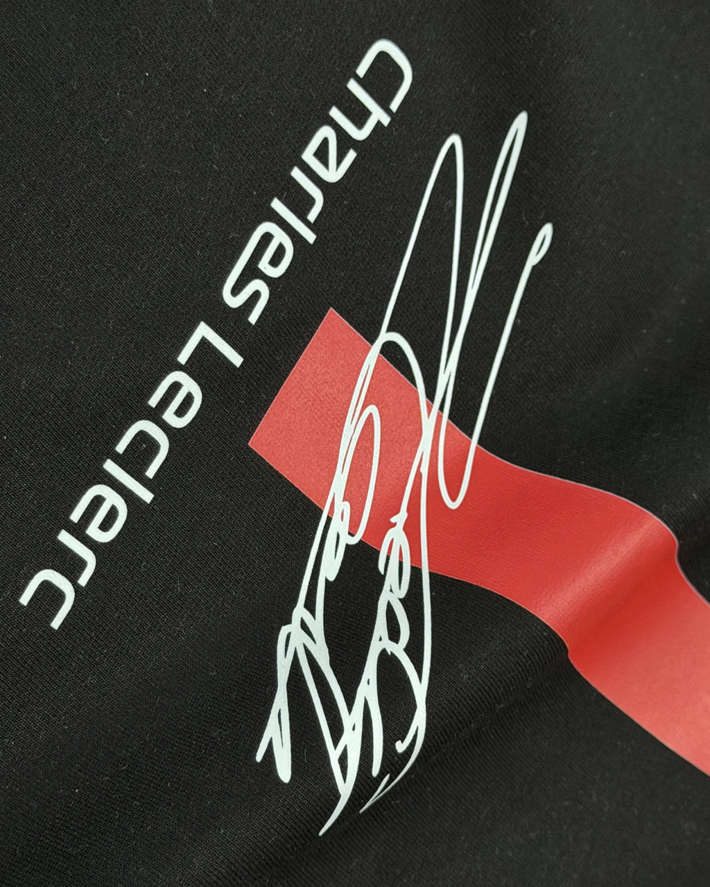 Closeup of F1 Black Unisex regular fit T-shirt by Turn 1 Brand, an F1 Apparel brand of India. Charles Leclerc fan tshirt with Front print features Ferrari logo and Charles Leclerc signature.