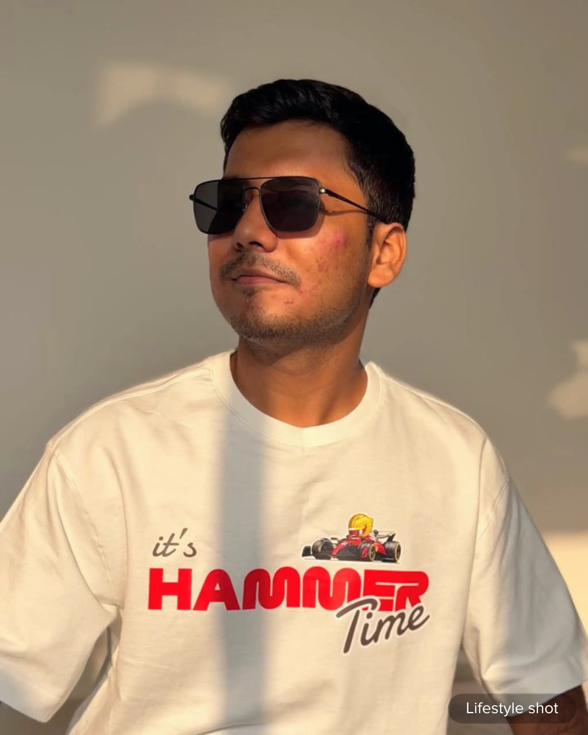 Lifestyle image of man wearing Lewis Hamilton It's Hammertime F1 Unisex Oversized T-shirt Off-White Front View Indoor Sunlit Background | Turn1 India