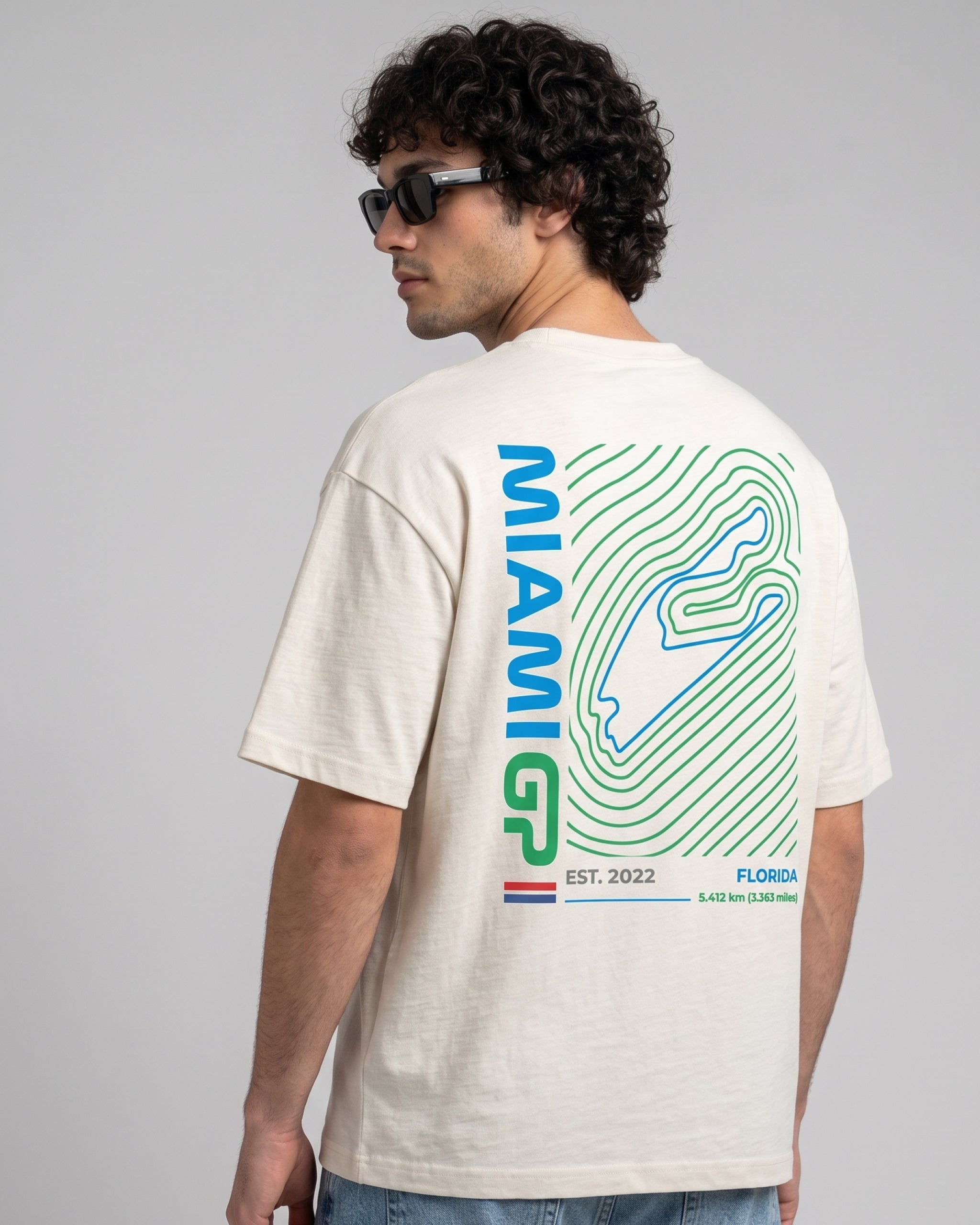 male model wearing Miami Florida USA Circuit F1 Turn1 India off white oversized unisex tshirt - with Miami circuit graphic